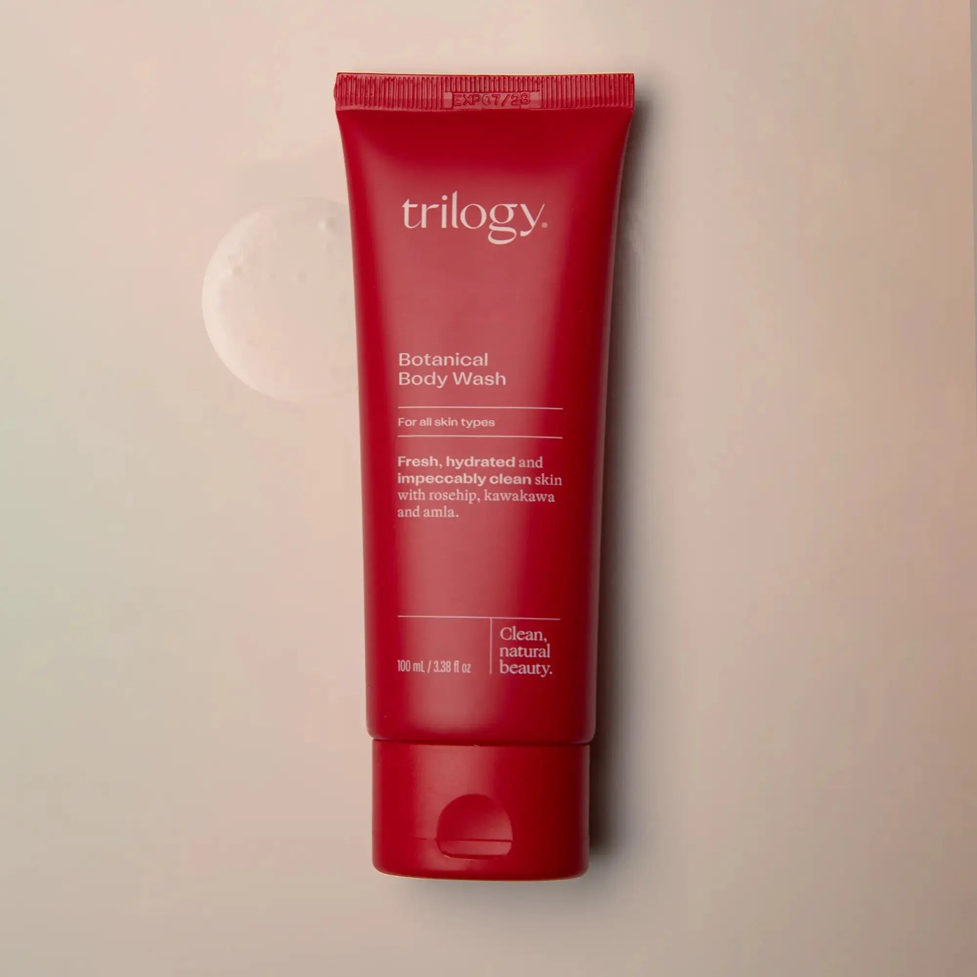 Red tube of Trilogy Botanical Body Wash on a beige background